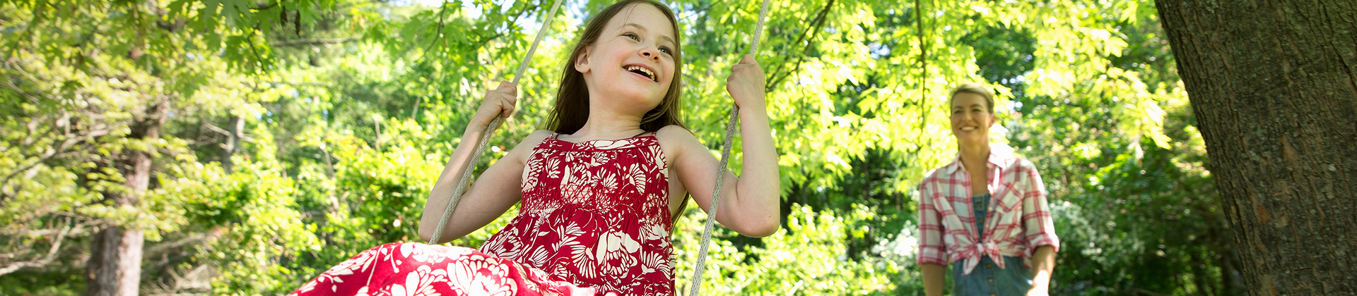 Child swinging in a wooded yard while an adult stands nearby
