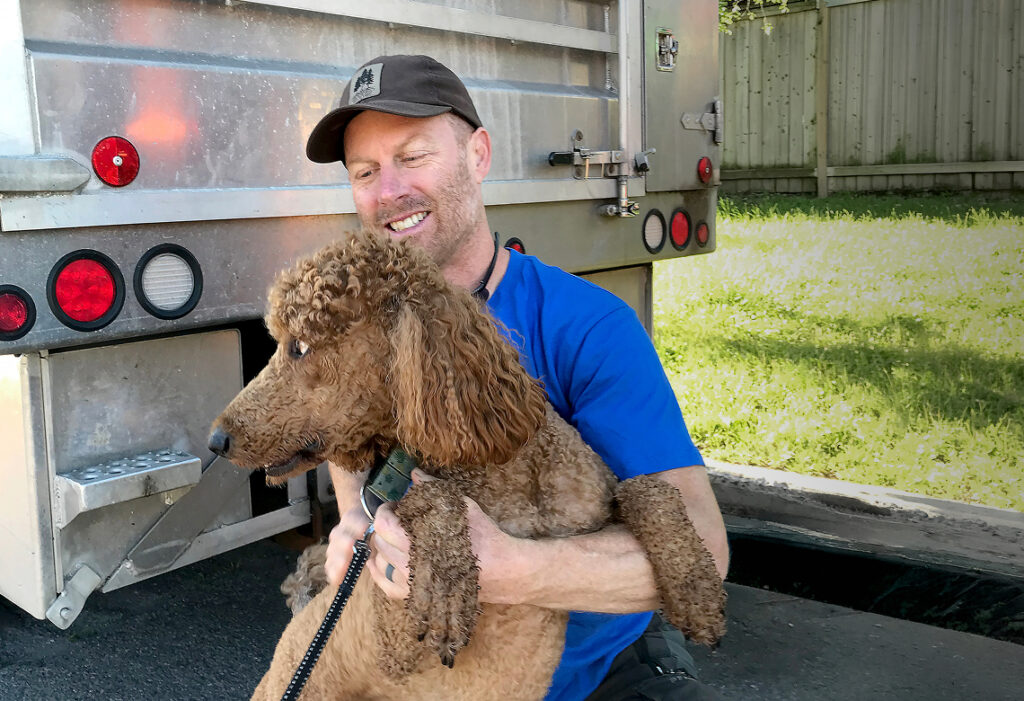 Man holding a curly brown dog beside a work truck